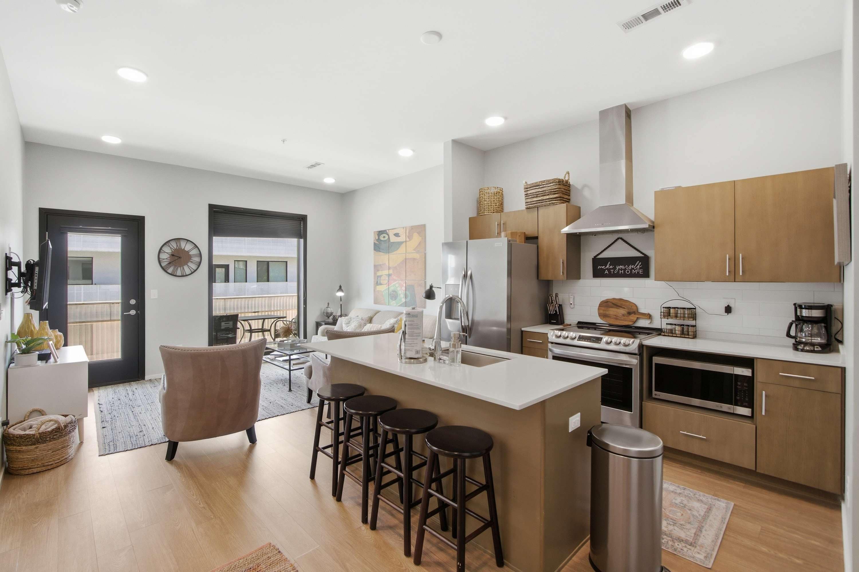 A modern kitchen with a central island, bar stools, wooden cabinets, and a stainless steel range hood.