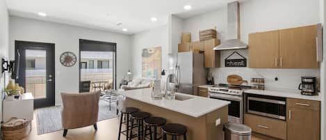 A modern kitchen with a central island, bar stools, wooden cabinets, and a stainless steel range hood.