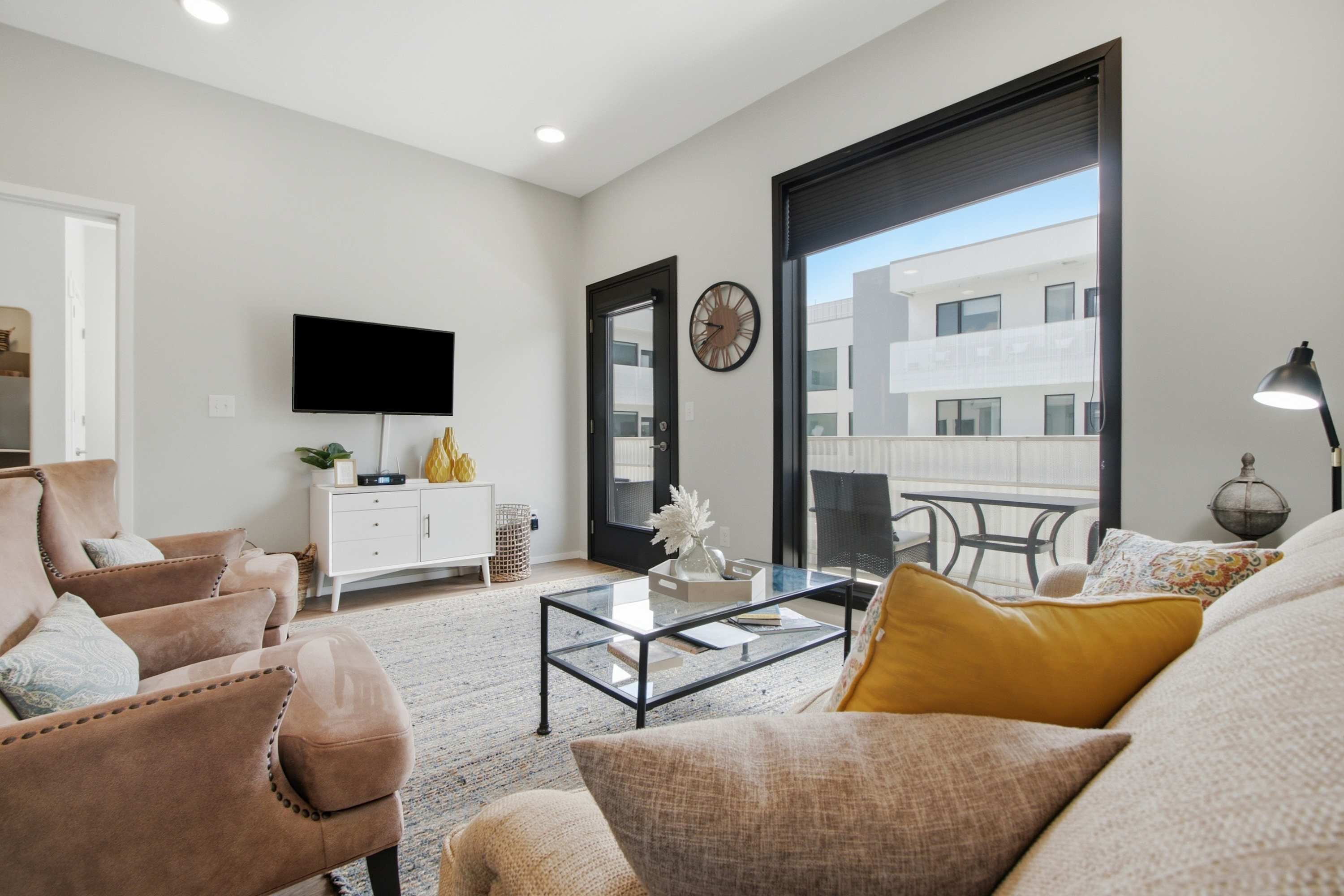 A living room with a sofa, armchair, coffee table, TV, and a view of a building through a large window.