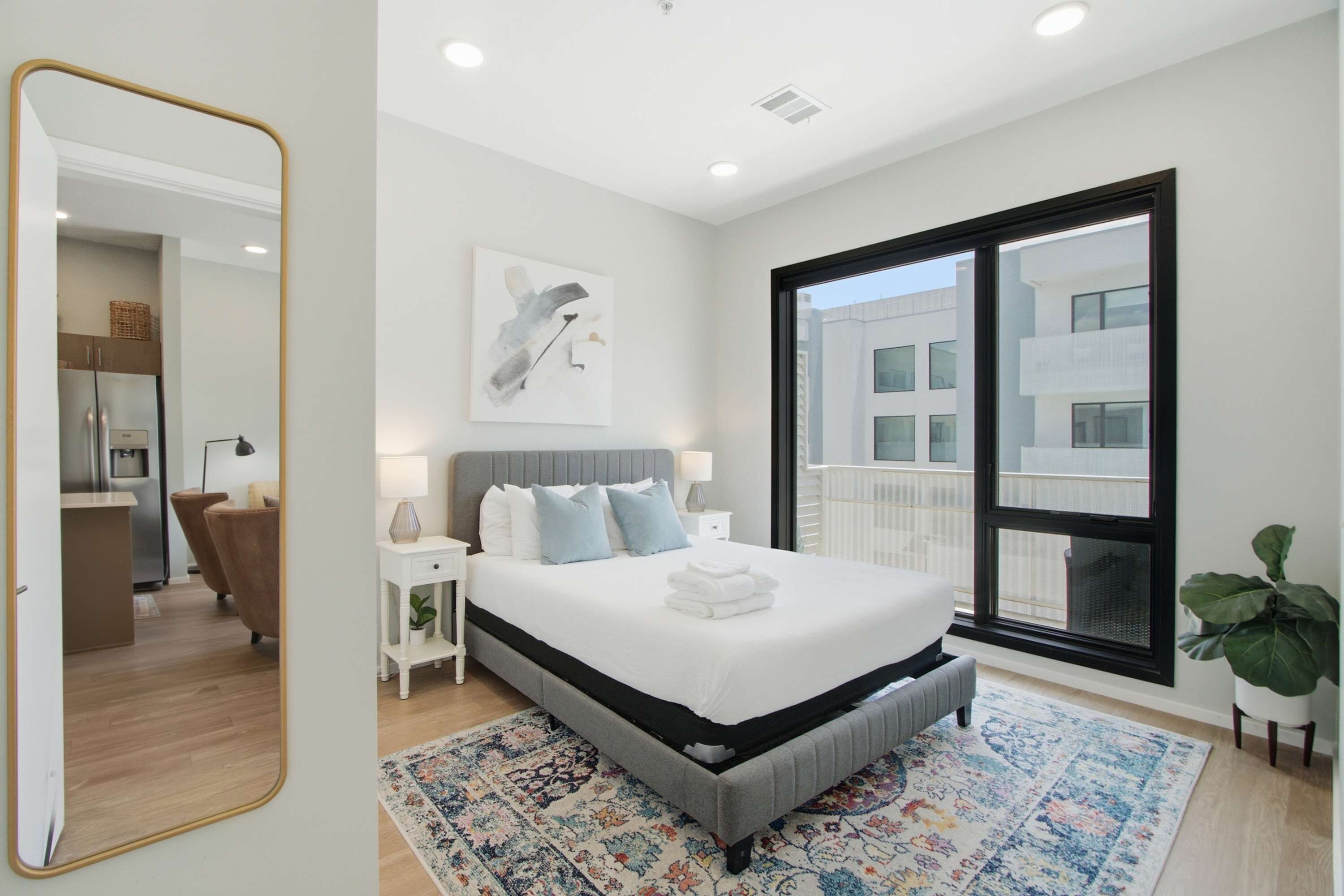 Een moderne slaapkamer met een groot bed, nachtkastjes, een spiegel en een stadszicht door een groot raam.