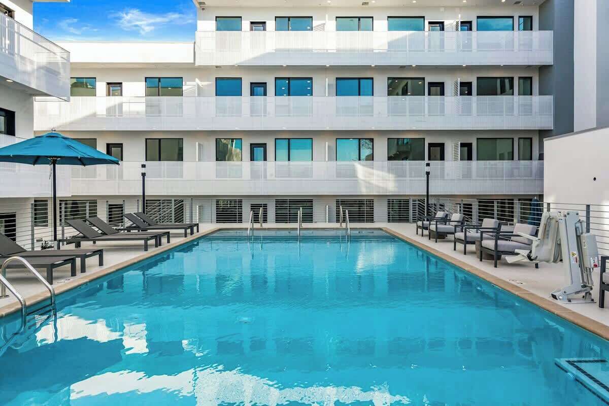 A modern hotel with a swimming pool, sun loungers, and a covered area with umbrellas.