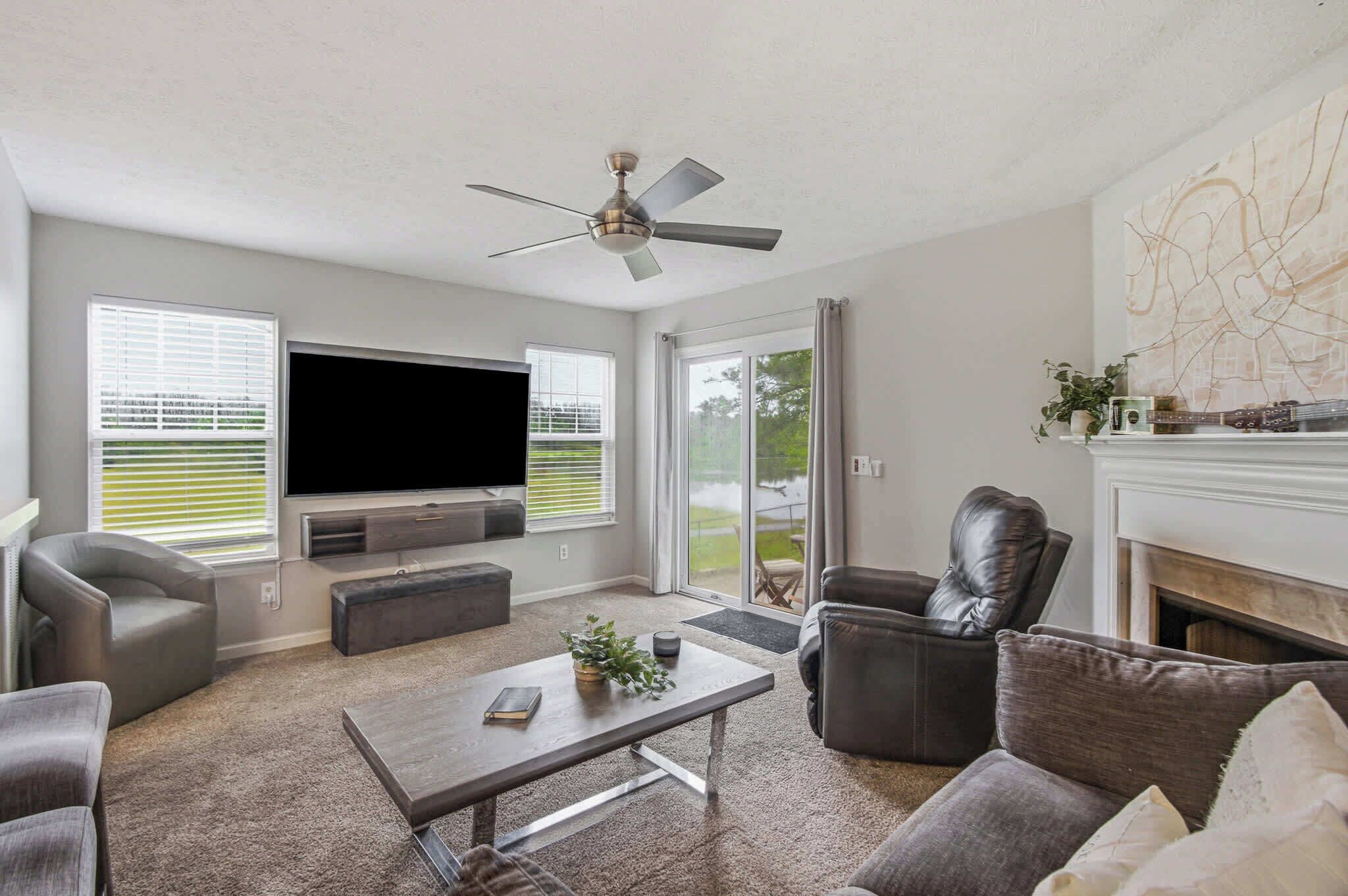 A living room with a flat-screen TV, a ceiling fan, a fireplace, and a large window.