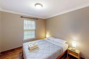 Habitació d'hotel amb un llit, abacines, una finestra amb persianes i un terra de fusta.
