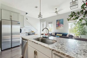 A modern kitchen with a stainless steel refrigerator, a granite countertop, and a built-in dishwasher. - Stylish townhouse with a rooftop deck, balconies, washer, dryer, & wet bar (Nashville)