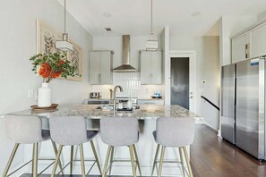 A modern kitchen with a central island, bar stools, stainless steel appliances, and a decorative vase. - Stylish townhouse with a rooftop deck, balconies, washer, dryer, & wet bar (Nashville)
