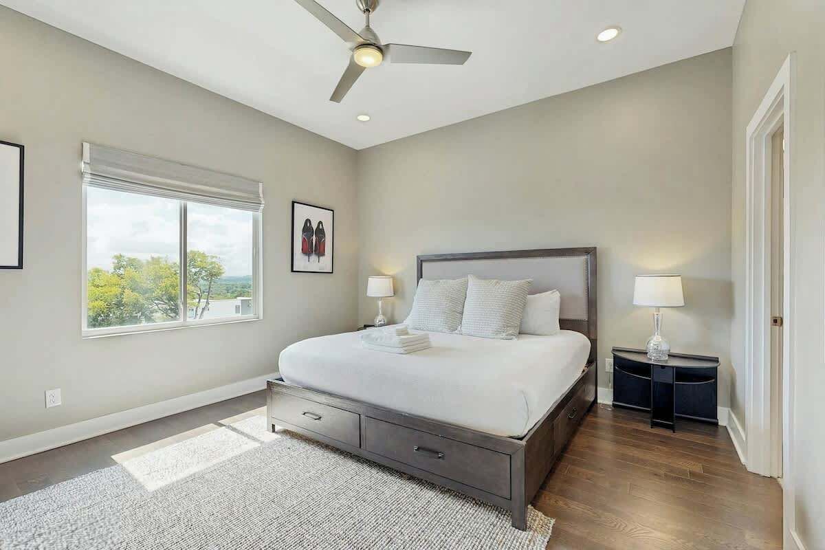 Un dormitorio con cama, ventilador de techo, ventana y mesita de noche.