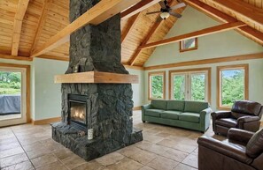 Ein geräumiges Wohnzimmer mit Kamin aus Stein, Holzbalkendecke, einem grünen Sofa und Ledersesseln.