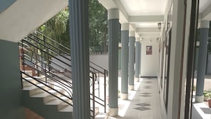 Un pasillo cubierto con suelo de baldosas, columnas y una escalera que conduce a un espacio al aire libre.