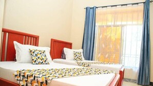 Habitación de hotel con dos camas, una ventana con cortinas azules y vista a árboles.