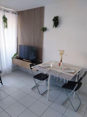A dining area with a table set for two, a television, and a window with curtains. - Cosy studio for 4 people private residence (Sète)