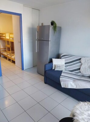 A modern living room with a blue sofa, a striped pillow, and a small plant on a tall cabinet. - Cosy studio for 4 people private residence (Sète)