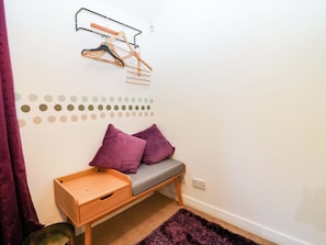 A small, neatly organized room with a wooden bench, two purple cushions, a metal drying rack, and a wall-mounted outlet. - Apartment 1 (Aberdeen)