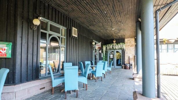 An outdoor seating area with stone flooring and blue chairs, a wooden ceiling, and a stone wall. - Apartment 1 (Aberdeen)