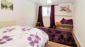 A bedroom with a bed, a window with curtains, a radiator, a hanging light fixture, and a wall-mounted shelf. - Apartment 1 (Aberdeen)