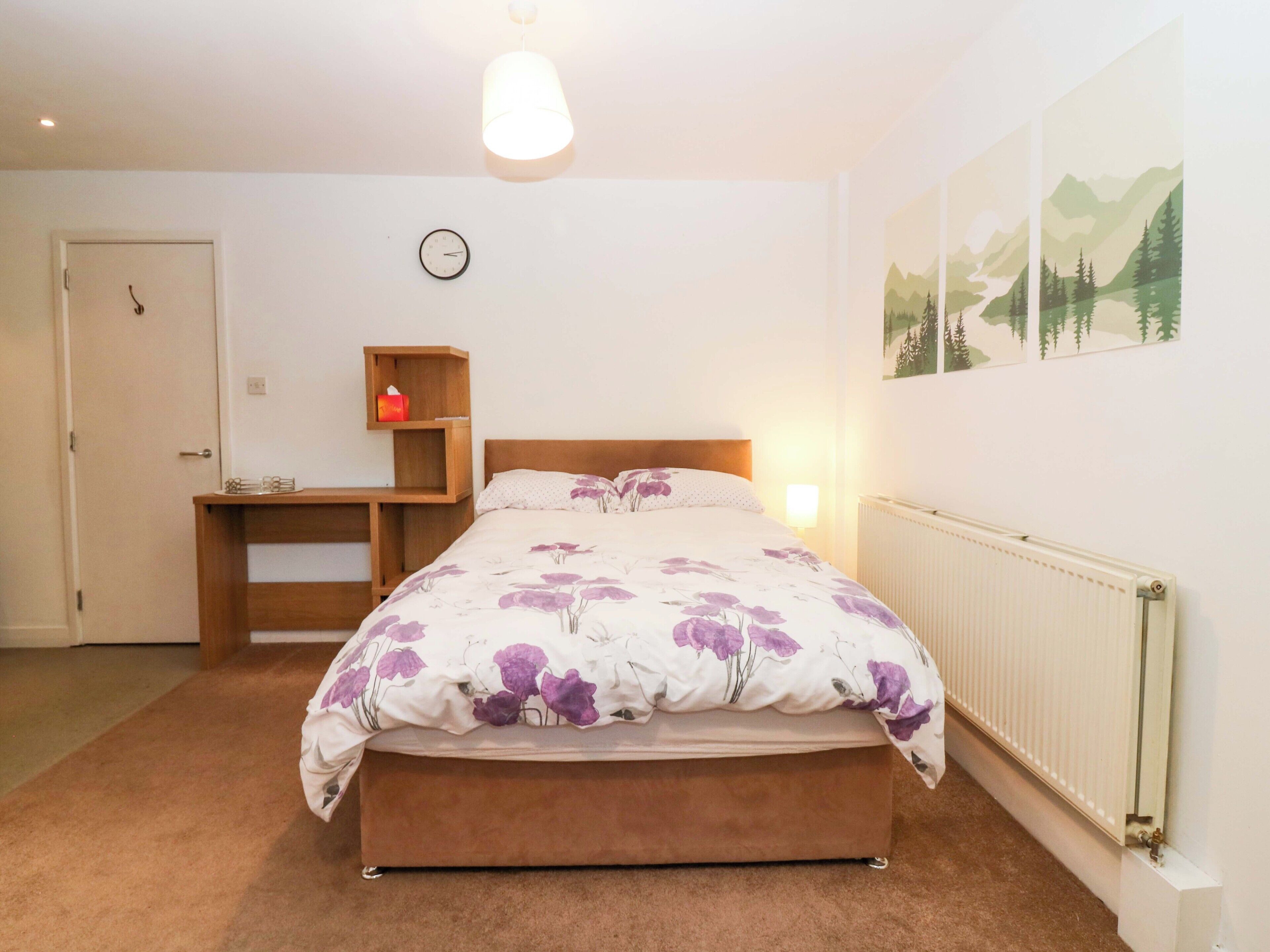 A bedroom with a bed, a bedside table, a clock, and a radiator.