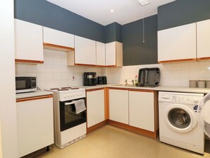 A compact kitchen with a microwave, stove, coffee maker, and washing machine. - Apartment 1 (Aberdeen)