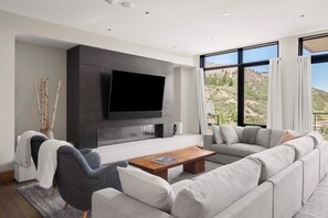 A modern living room with a large flat-screen TV, a grey sectional sofa, a wooden coffee table, and a fireplace. - One Snowmass East 603 (Snowmass Village)