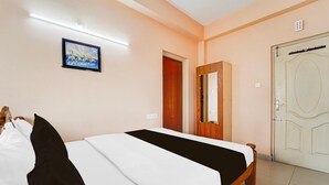 A hotel room with a bed, a door, a mirror, and a painting on the wall. - Deluxe Viswa Towers (Madurai)
