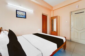 A hotel room with a bed, a door, a mirror, and a painting on the wall. - Deluxe Viswa Towers (Madurai)
