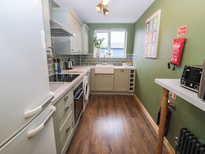 A compact kitchen with white cabinets, a stove, and a sink. - Home by the sea (Llandudno)