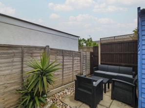 A patio area with a seating arrangement, a potted plant, and a wooden fence. - Home by the sea (Llandudno)