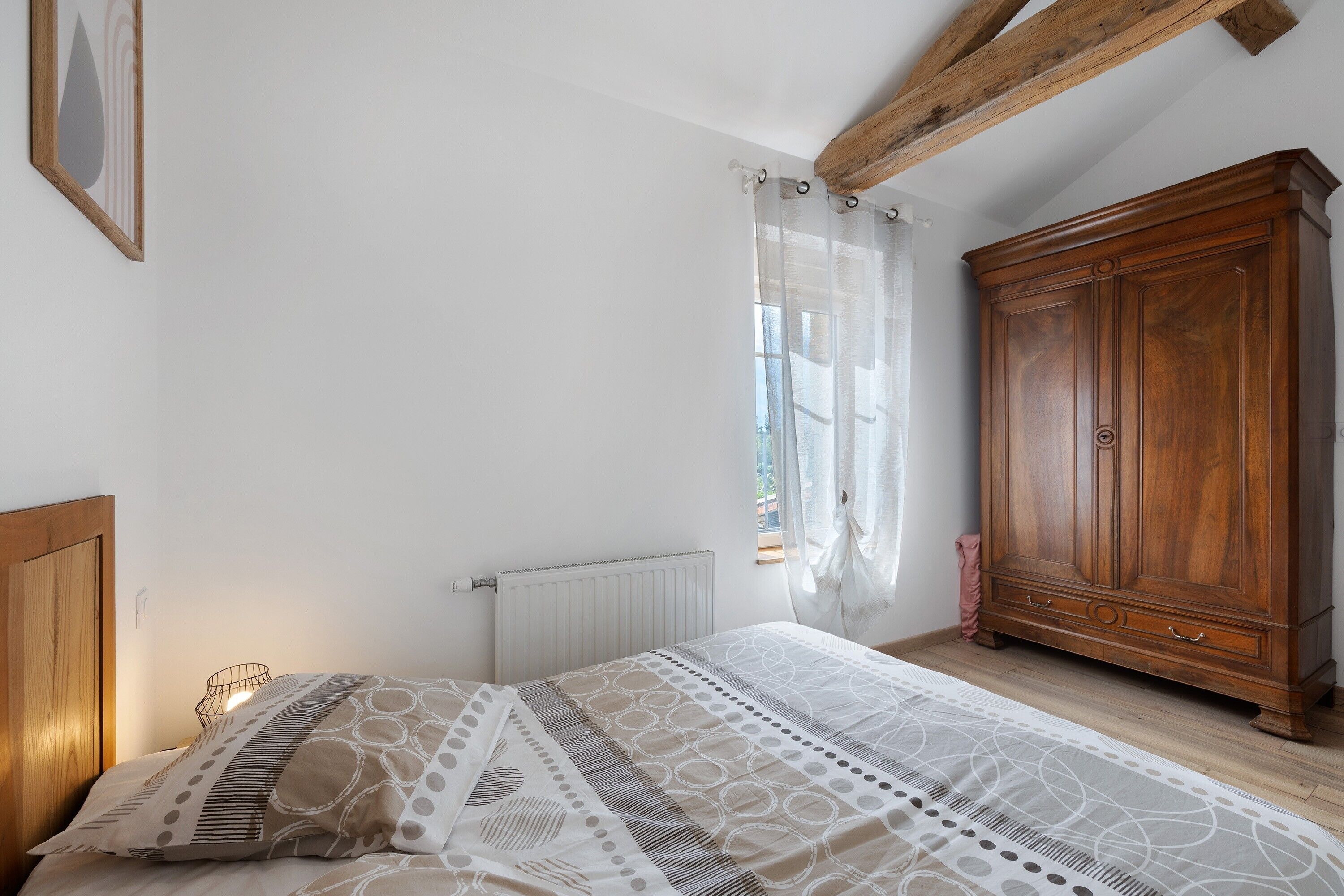 A bedroom with a bed, a wooden wardrobe, a radiator, and a window with curtains.