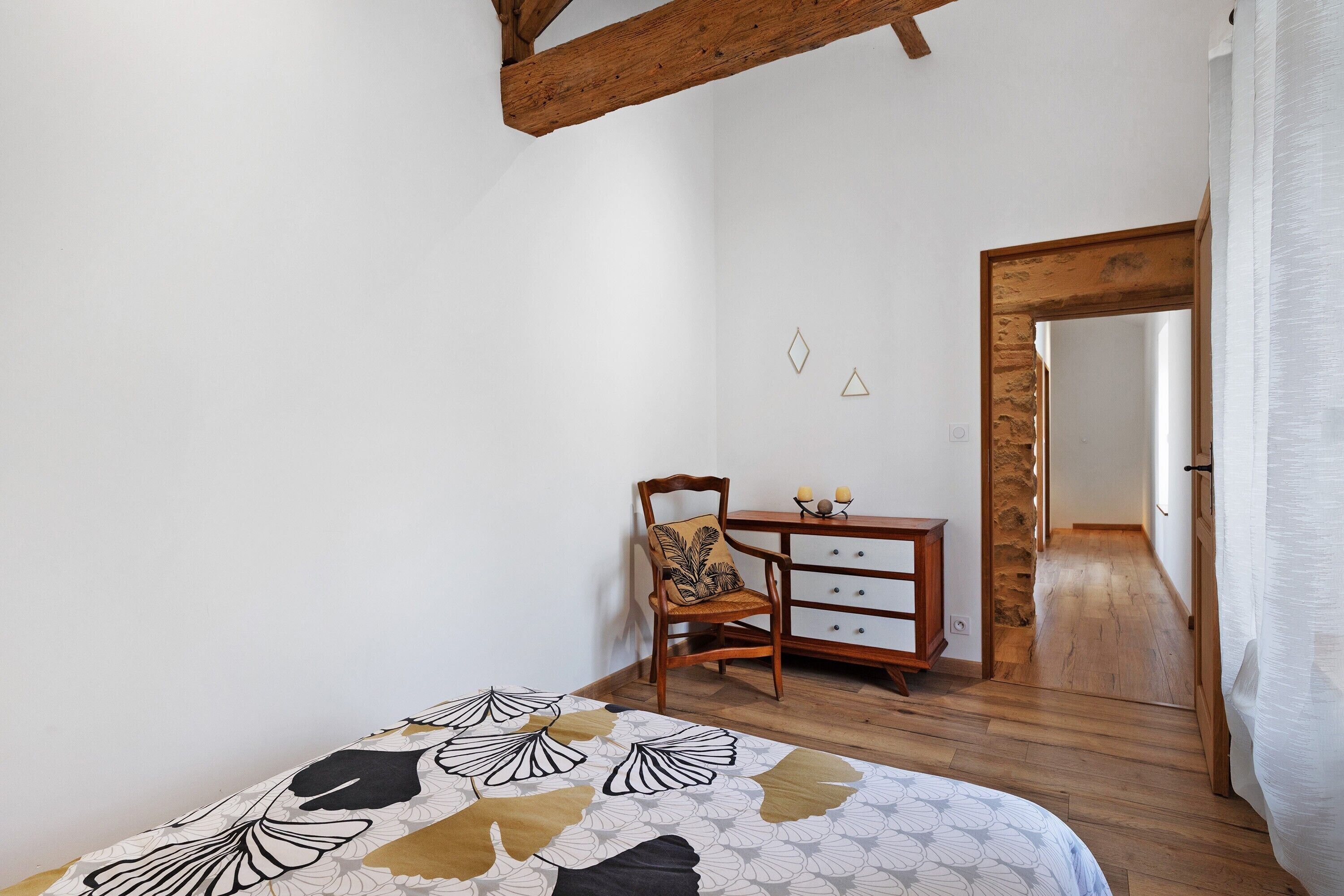 Een slaapkamer met een bed, een houten stoel, een kast en een stenen muur.