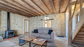 A rustic interior with exposed wooden beams, a stone wall, a grey sofa, a wooden coffee table, and a staircase. - Le Clos des Prés with Pool, Spa and Table Football (Rives de l'Yon)