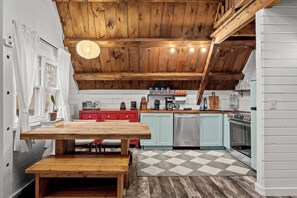 Een keuken met houten balken, een houten tafel, een rode kast en een geruit tapijt.
