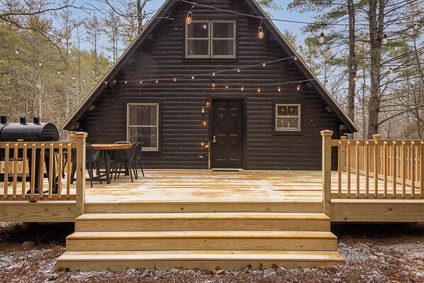 A cabin with a wooden deck, a barbecue grill, and string lights.