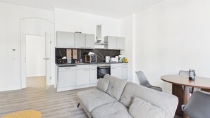 A modern kitchen with white cabinets, a built-in oven, and a dining area with a round table and chairs. - Family apartment with balcony, up to 5 guests - GÖ04 (Görlitz)