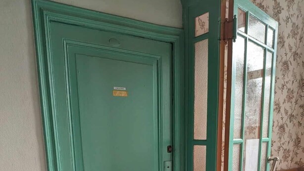 Una porta color petrolio con un piccolo oblò e un tappetino.