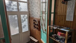 A room with a wooden door, a window, a small bench, and a shelf with board games.