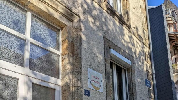 A building with a white door, a window with a black balcony, a sign reading 'Les Nids Douillets,' and a red mailbox.