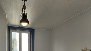 A room with a bed, a table, a chair, a window, and a hanging light fixture.