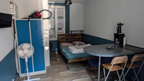 A compact room with a bed, a dining table, a fan, and a kitchenette.