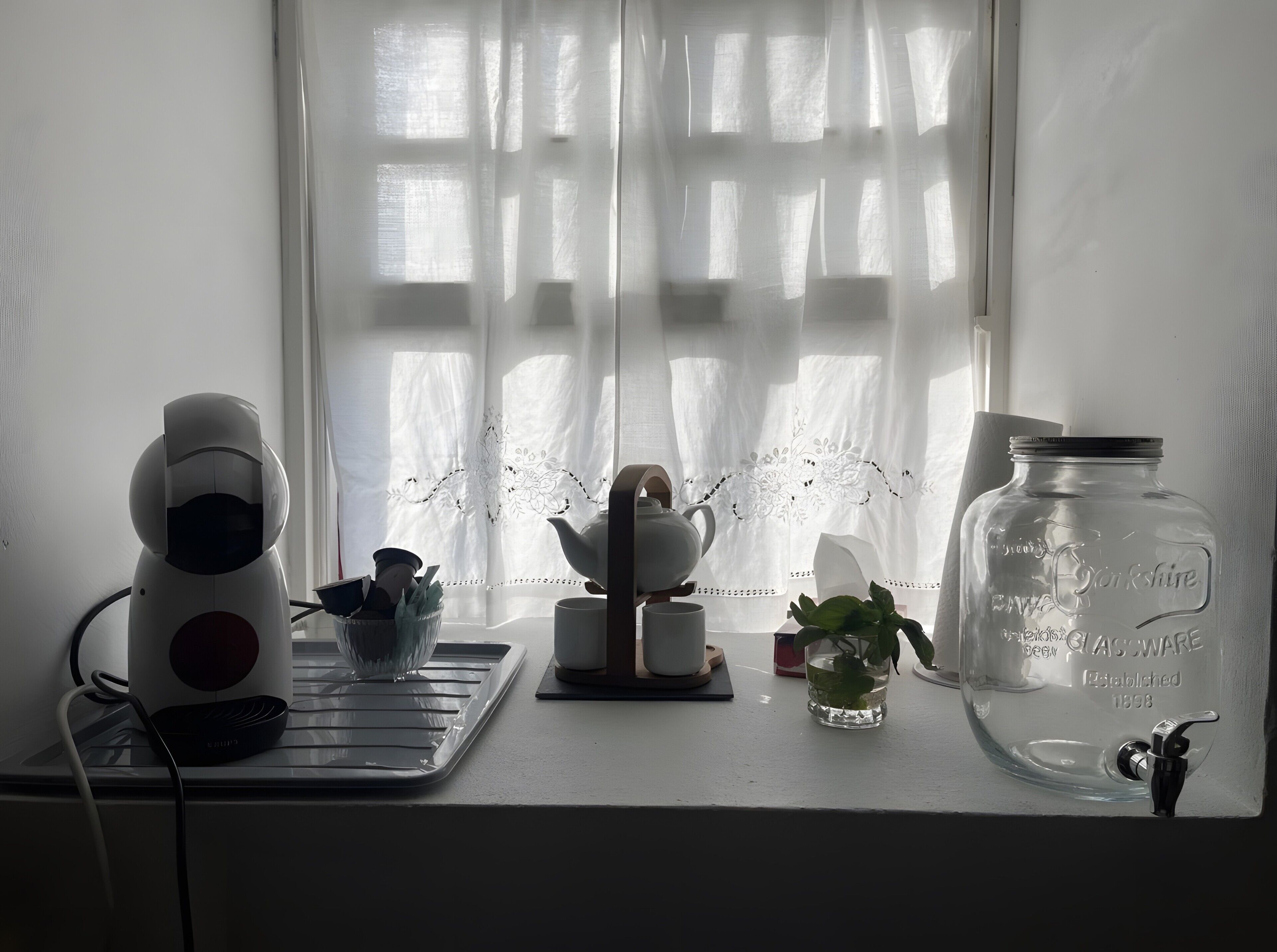 Een keukentafel met een koffiezetapparaat, een theepot, een glazen pot en een kleine plant.