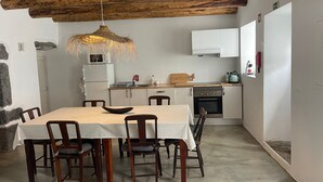 A dining area with a table and chairs, a hanging light fixture, a kitchen with appliances, and a stone wall. - Holiday Home 'Casa Baía Da Lagoa' with Sea View and Wi-Fi (Lagoa)