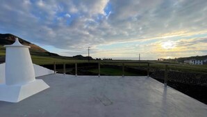 A concrete deck with a white structure, a grassy field, and a cloudy sky. - Holiday Home 'Casa Baía Da Lagoa' with Sea View and Wi-Fi (Lagoa)