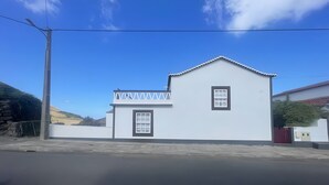 A single-story house with a white exterior, a small balcony, and a single window. - Holiday Home 'Casa Baía Da Lagoa' with Sea View and Wi-Fi (Lagoa)
