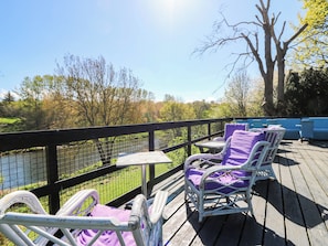 Una terraza con mobiliario exterior, vista a un río y árboles al fondo.