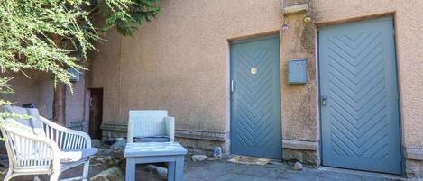 Une cour avec un banc, deux portes et un mur en pierre.