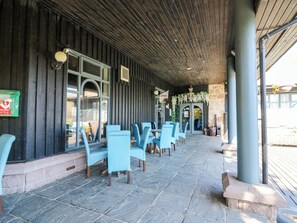An outdoor seating area with stone flooring and blue chairs, a wooden ceiling, and a stone wall.