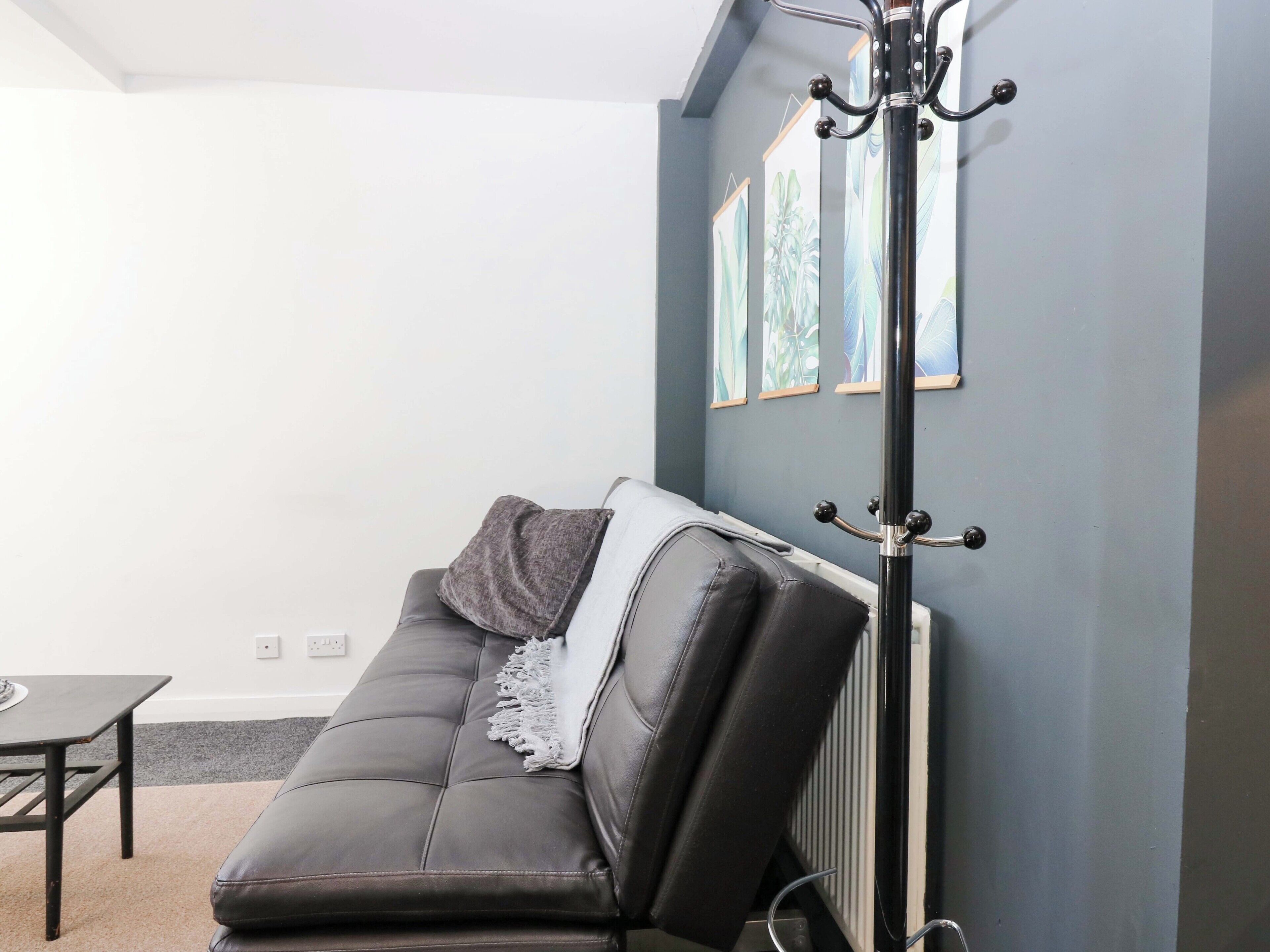 A modern living room with a black leather sofa, a small table, and a radiator.