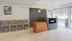 A reception desk with a sign, chairs lined up, a clock, and a large window. - Townhouse Oak Sevoke Road Siliguri (Jalpaiguri)
