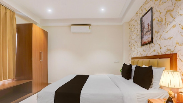 A hotel room with a bed, bedside table, lamp, air conditioning unit, wardrobe, and a framed picture on the wall. - Townhouse Oak Sevoke Road Siliguri (Jalpaiguri)