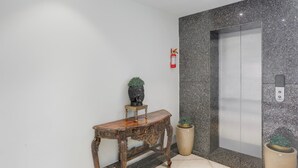 A lobby with a marble wall, a wooden console table, a potted plant, a fire extinguisher, and an elevator. - Townhouse Oak Sevoke Road Siliguri (Jalpaiguri)