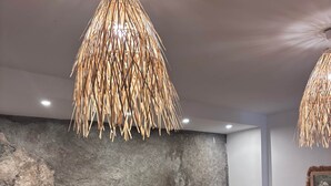 A room with a rock wall, two wicker chairs, a small table with a vase, and a hanging light fixture.