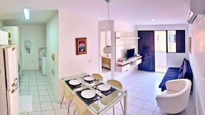 Un apartamento moderno con comedor, sala de estar con sofá y televisor, y cocina equipada.