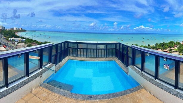 Una piscina con vistas al océano y la playa, rodeada de barandillas de vidrio.